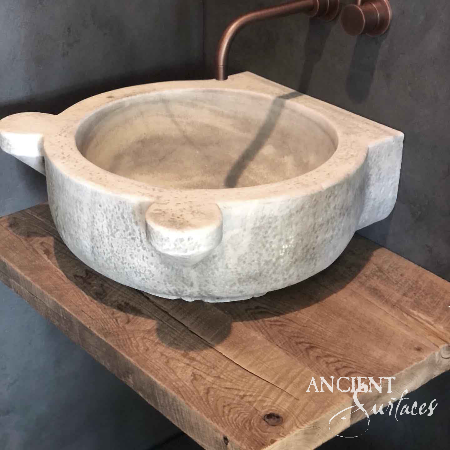 Antique marble vessel sink from Ancient Surfaces with carved lug handles on a reclaimed oak shelf beneath a copper faucet
