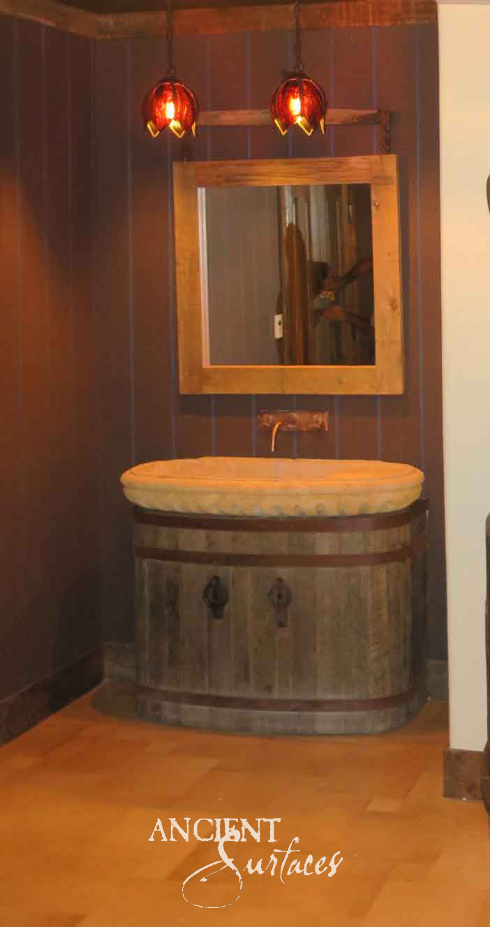 Carved golden limestone oval basin from Ancient Surfaces with a beaded rim on a rustic barrel vanity