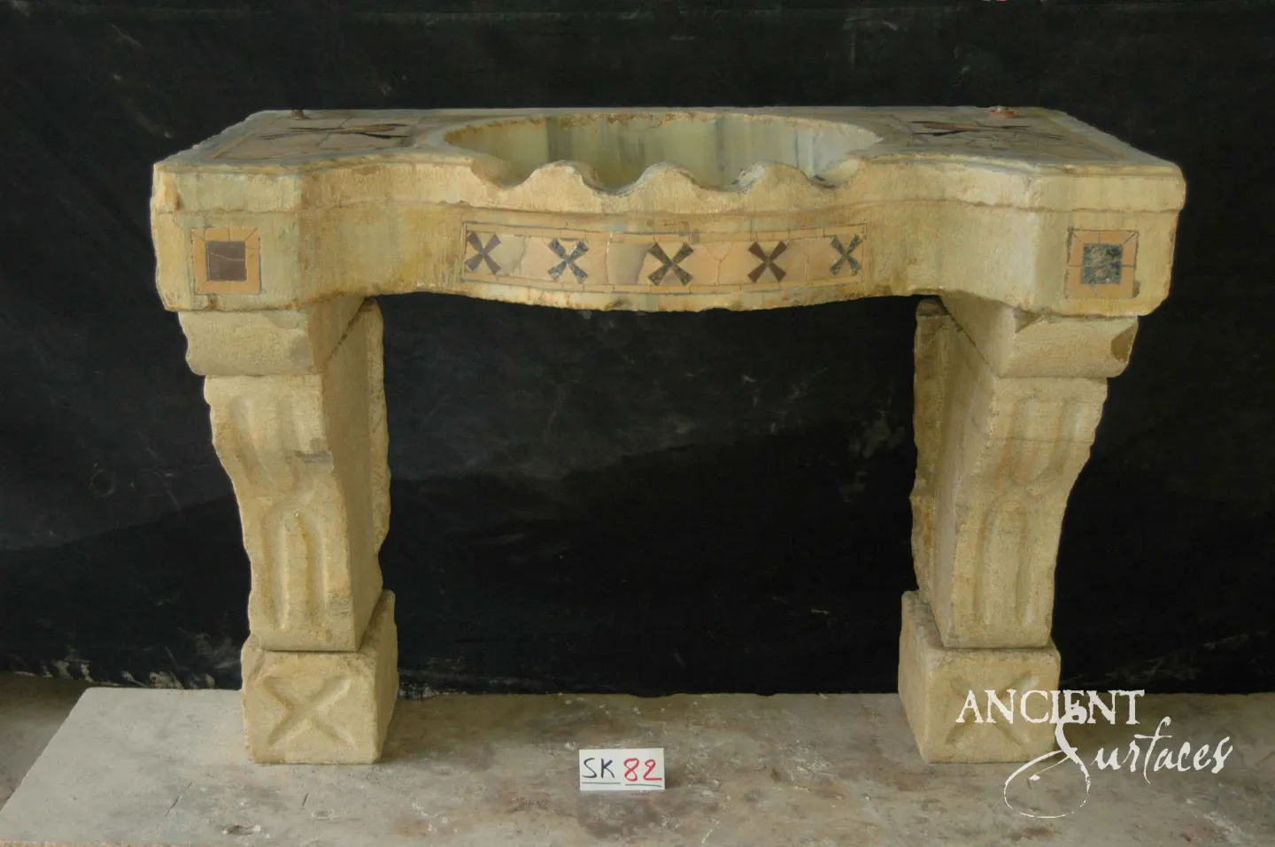 Golden limestone console sink from Ancient Surfaces with a scalloped basin and a cross patterned mosaic apron band