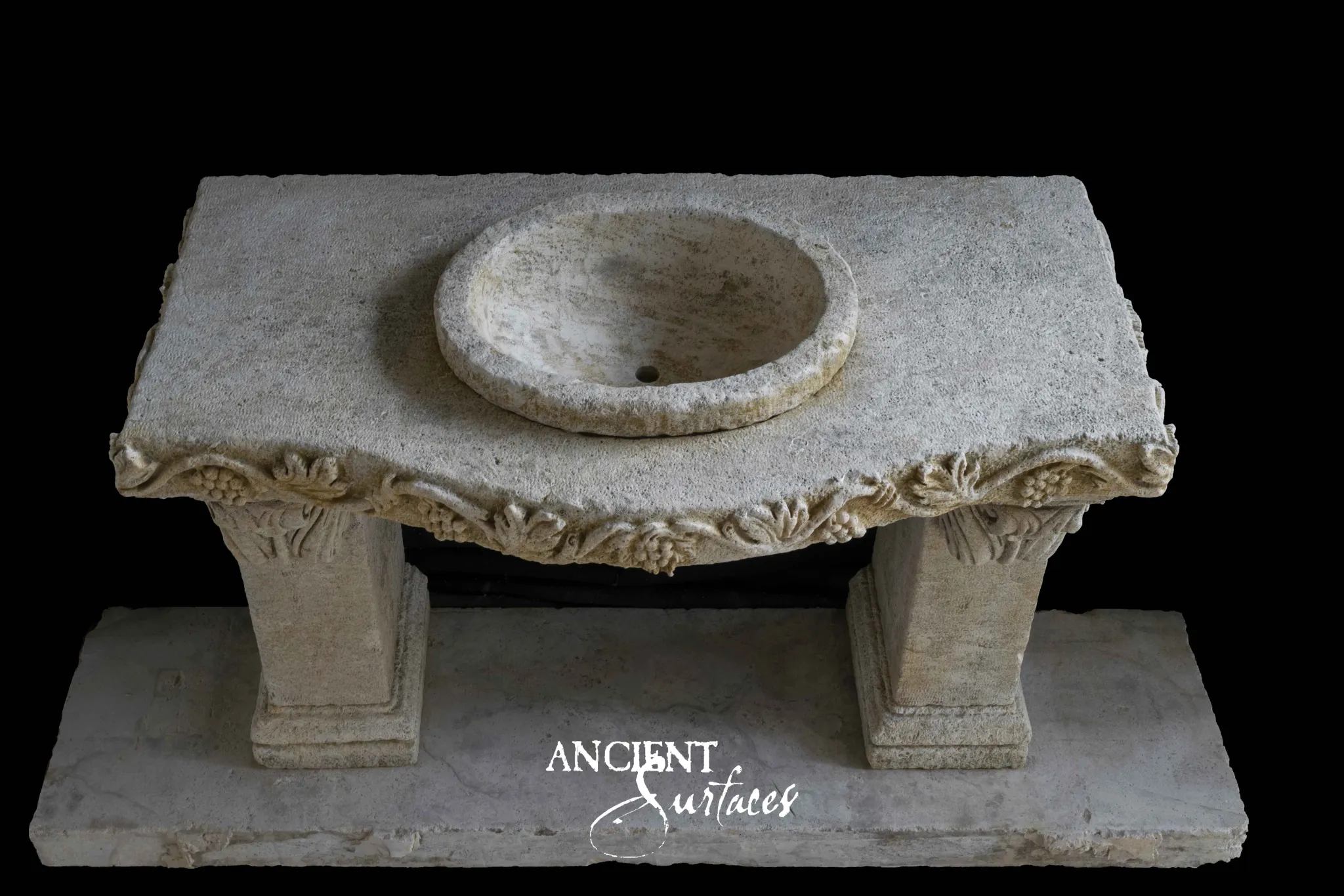 Carved limestone console sink from Ancient Surfaces with a deep grapevine apron and a raised round basin on tapered pedestals